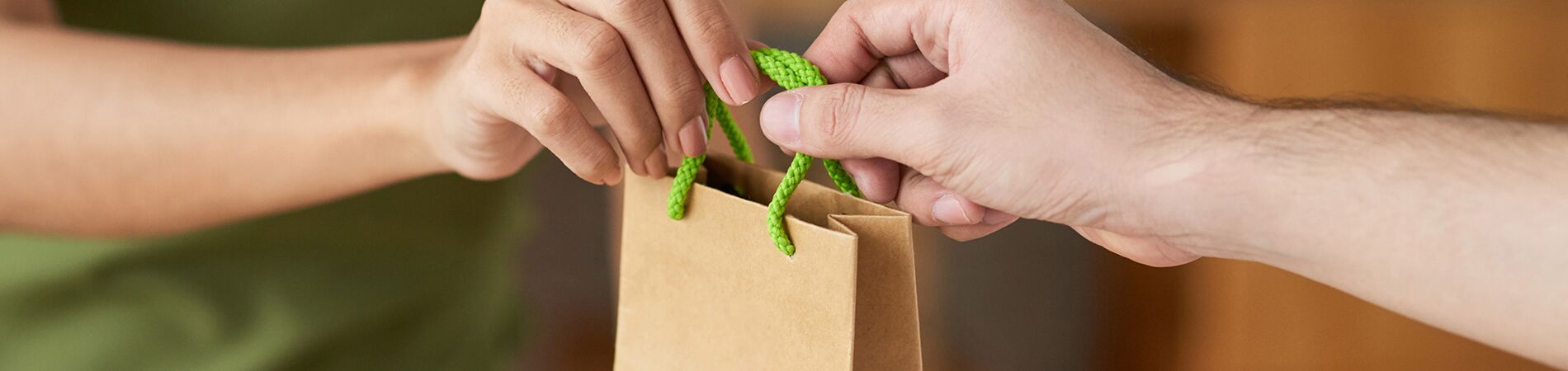 Zwei Hände übergeben eine nachhaltige Papiertüte – Symbol für bewussten Konsum und Kreislaufwirtschaft